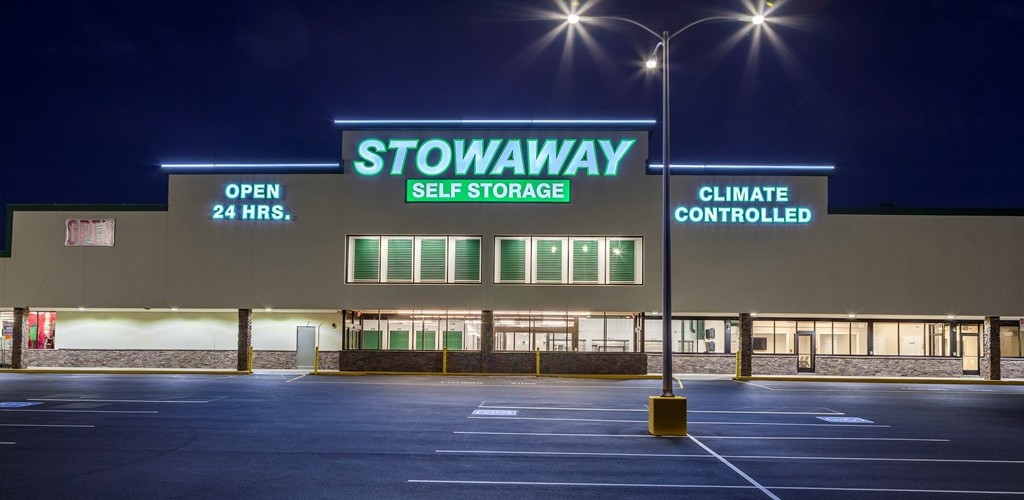 Two story conversion of a former retail store, featuring a bright white hall system with evergreen doors. Lighted signage and windows showing doors advertises this site as a self-storage facility.