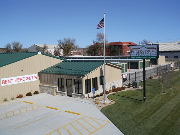 Classic beige self-storage buildings with evergreen roof and trim, featuring integrated rental office with 24 hour kiosk in office.