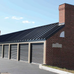 Classic beige self-storage building with matte black doors. Featuring custom brick walls with
architectural chimney and window accents to complement neighboring structures.