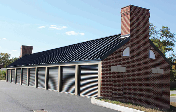 Classic beige self-storage building with matte black doors. Featuring custom brick walls with
architectural chimney and window accents to complement neighboring structures.