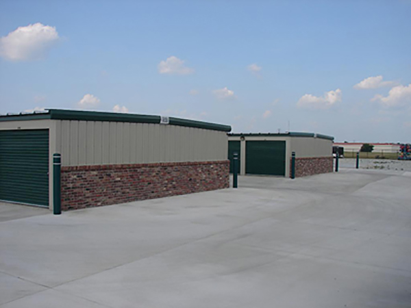 Slate gray self-storage buildings with evergreen trim and doors, featuring brick end wall Wainscotting.
